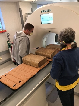 man and woman on either side of a book on a conveyor belt going into a CT scanner